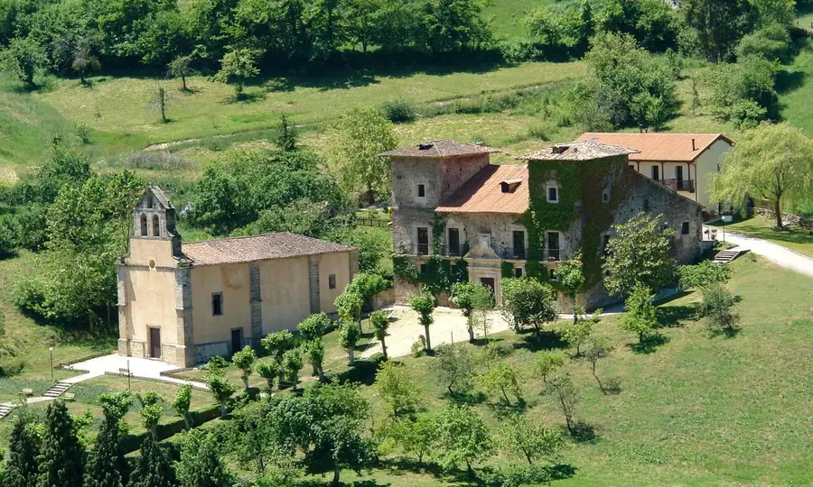 Vista aérea del Palacio del Marqués de Casa Estrada: el cuerpo de piedra con la fachada cubierta de hiedra, una capilla junto a él y prados y arbolado alrededor
